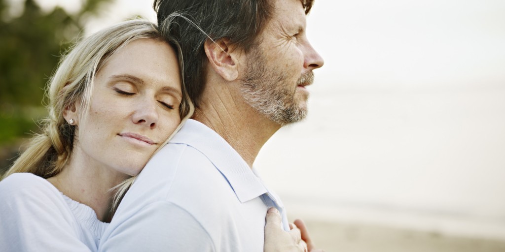 Wife embracing husband on beach at sunset